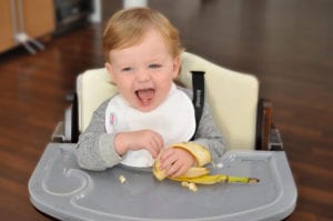 a baby laughing while holding a banana and wearing a Bibby bib