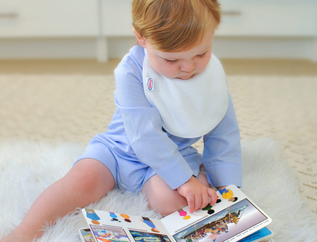 a baby reading a book wearing a Bibby bib