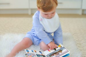 a baby reading a book wearing a Bibby bib