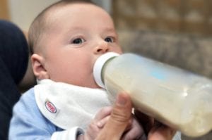 a baby drinking a bottle wearing a Bibby bib