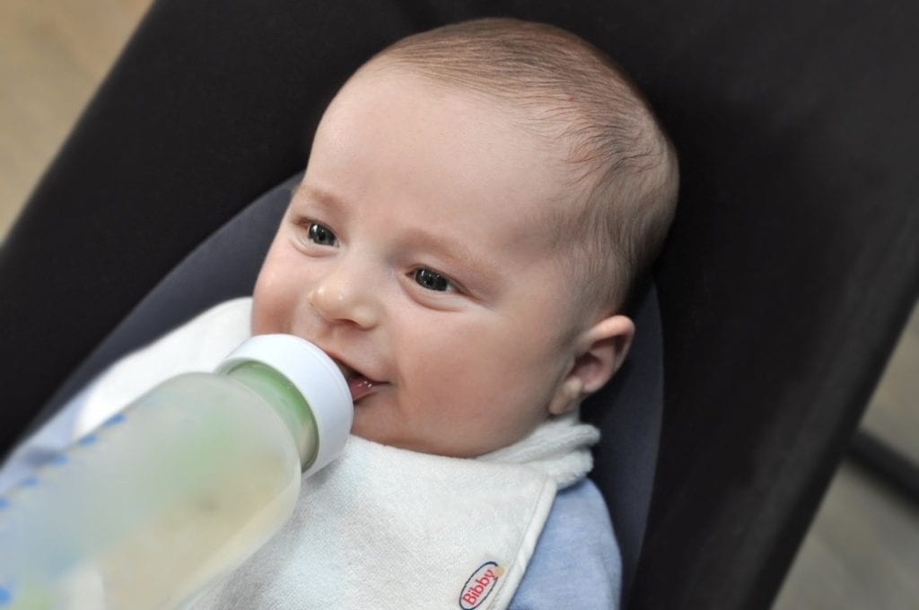 baby smiling and drinking a bottle, wearing a Bibby bib