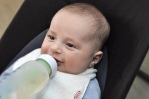 a smiling, dry baby eating from a bottle in a Bibby collared bib